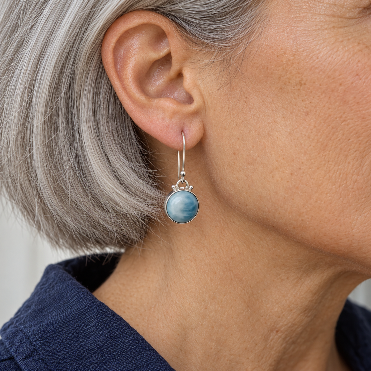 Round Larimar sterling silver drop earring worn by a woman with silver hair and navy linen.