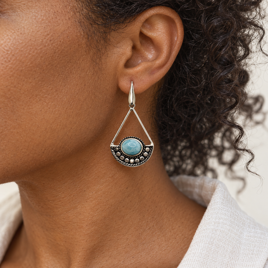 Triangular Larimar sterling silver drop earring worn by a woman with curly dark hair and ivory linen.