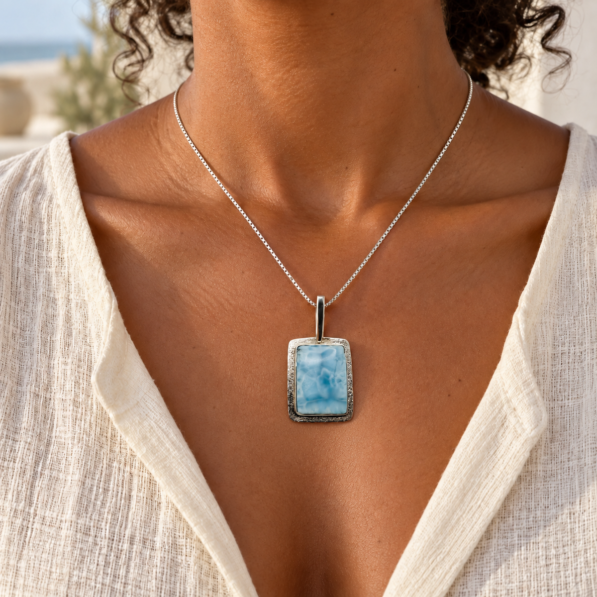 Woman in cream linen wearing a rectangular Larimar necklace at 1.1 inches wide by 1.7 inches high