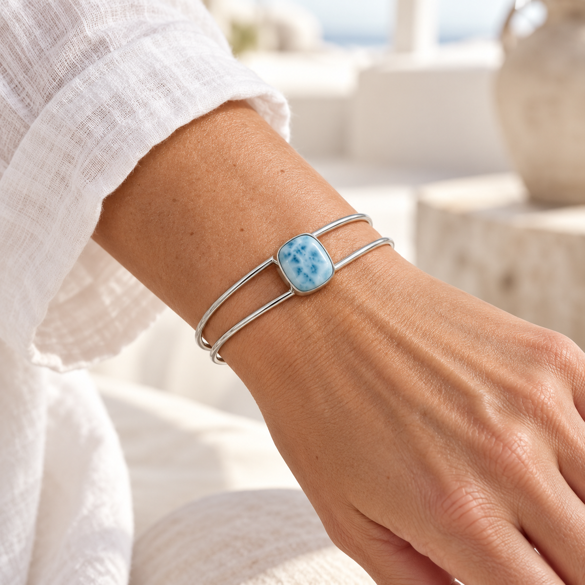Cushion-shaped Larimar sterling silver double-wire cuff bracelet worn on a woman’s wrist with a white linen sleeve