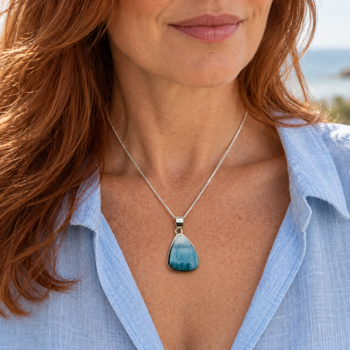 Auburn-haired woman wearing a teardrop Larimar necklace at 1 inch wide by 1.6 inches high