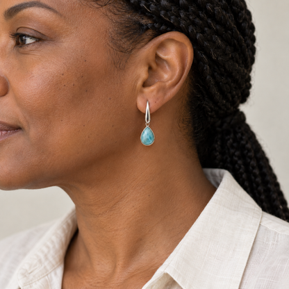 Model with braided hair and an ivory linen shirt wearing pear-shaped Larimar earrings; approximate scale mockup.