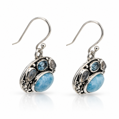 Angled view of ornate oval Larimar earrings with polished sterling silver scrollwork and dark recessed finish.