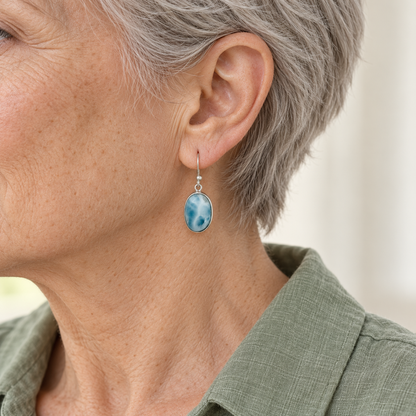 Silver-haired model wearing an oval Larimar earring with a sage linen shirt; approximate size mockup.