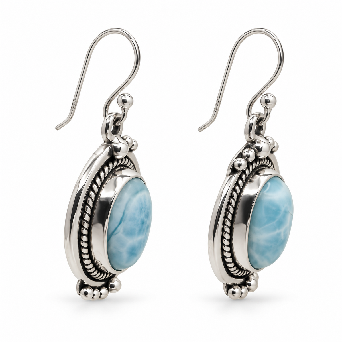 Angled view of oval Larimar earrings showing rope borders, silver bezel depth and fishhooks on white.