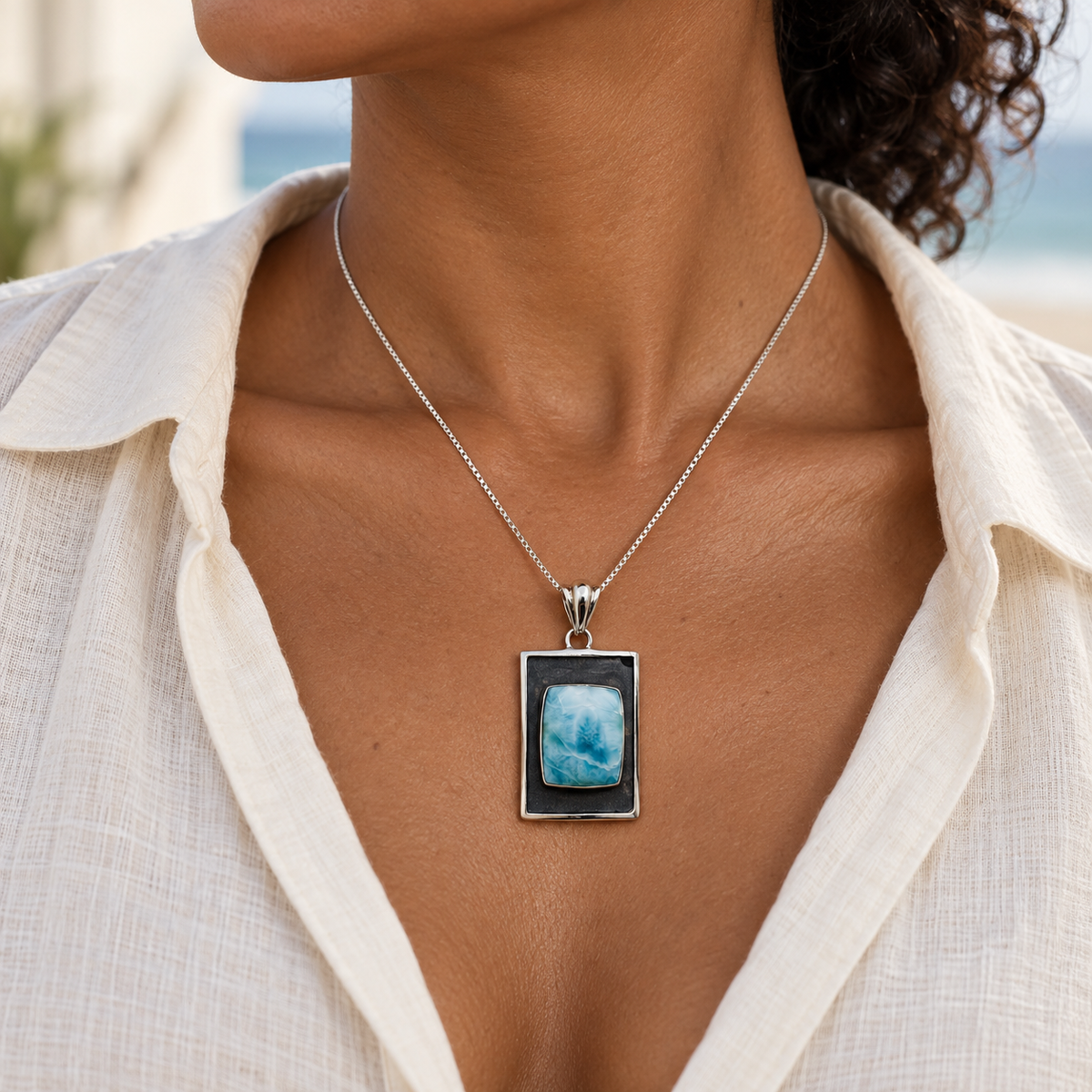 Dark-complexioned woman in cream linen wearing the Ocean Tableau Larimar necklace