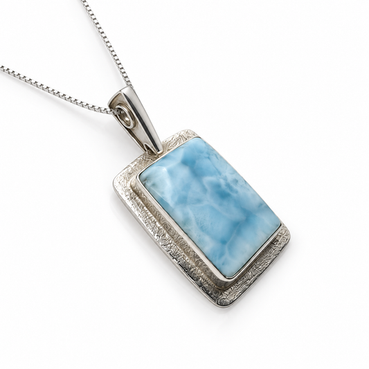 Rectangular Larimar necklace with textured sterling silver frame, angled view on glossy white