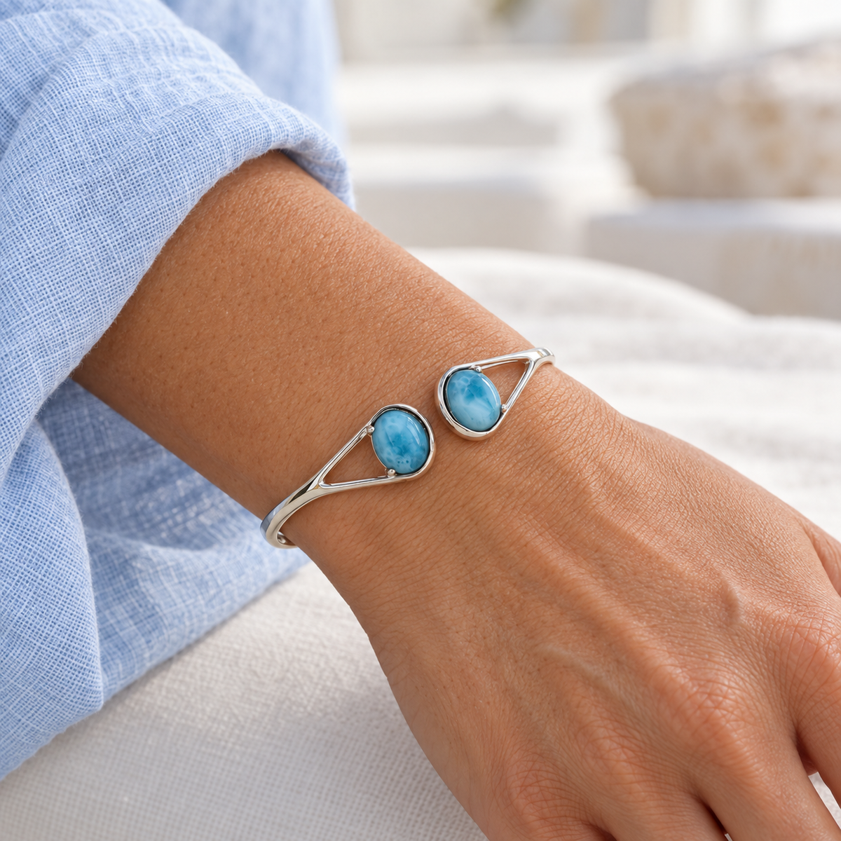 Two-stone Larimar sterling silver bypass cuff bracelet worn on a woman’s wrist with a pale blue linen sleeve
